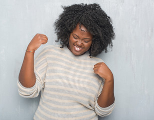 Young african american plus size woman over grey grunge wall wearing a sweater very happy and...