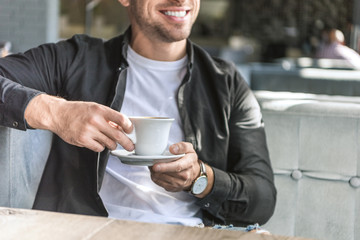cropped shot of young man with cup of coffee sitting in cafe