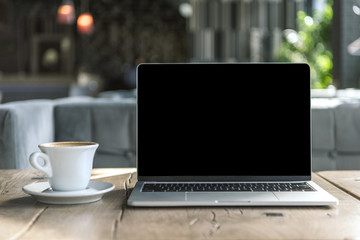 cup of delicious coffee and laptop with blank screen on rustic wooden table at cafe