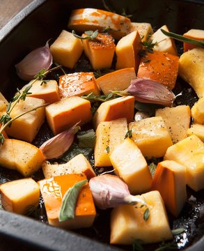Close up of pumpkin pieces with garlic, sage and thyme in tray