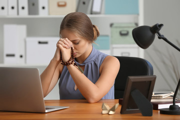 Beautiful young woman praying in office