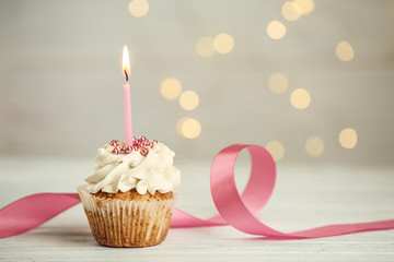 Delicious birthday cupcake with burning candle on light table