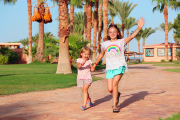 Happy sisters run on footpath in tropical resort. Sisters relaxing on vacations