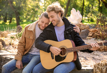 Happy gay couple with guitar in park