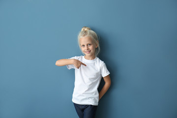 Cute little girl pointing at her t-shirt on color background