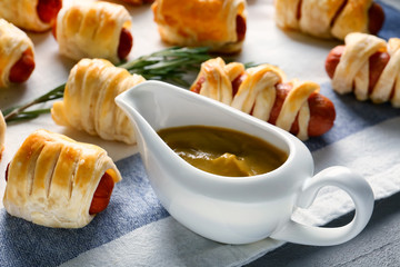 Tasty sausage rolls and gravy boat with sauce on table