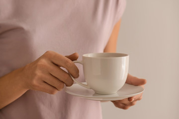 Woman holding cup of aromatic coffee on light background, closeup