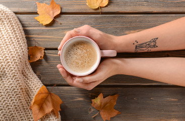 Female hands with cup of aromatic coffee on wooden background, top view