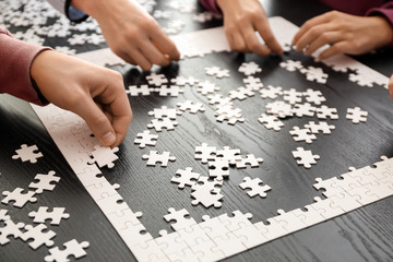 Group of people assembling puzzle on dark table