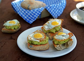 Healthy breakfast, toast with avocado mash and fried quail egg on a brown background.
