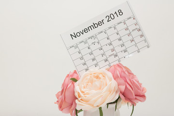 Calendar of November 2018 with holiday date of Thanksgiving Day and lunar days is on above bouquet of pastel-colored flowers on white background. 