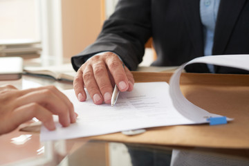 Close-up of businessman examining business contract and signing it at the office desk - obrazy, fototapety, plakaty