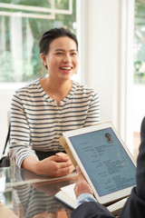 Female employee smiling during job interview, manager examining her resume on touchpad