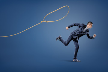A businessman in a suit runs away from a rope lasso that tries to catch him.