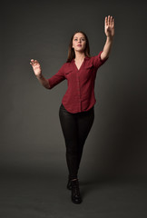 full length portrait of brunette girl wearing  red shirt and leather pants. standing pose, on grey studio background.