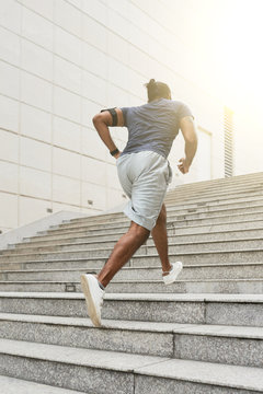 Unrecognizable athletic man in sportswear running up concrete stairs outdoors while having daily morning workout, rear view