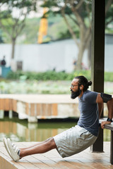 Side view of concentrated bearded Indian male athlete listening to music through earbuds while working out outdoors