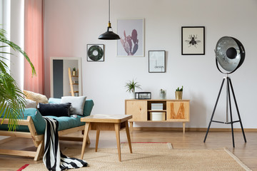 Eclectic apartment with industrial lamp, sofa with pillows, wooden table and posters on the wall, real photo