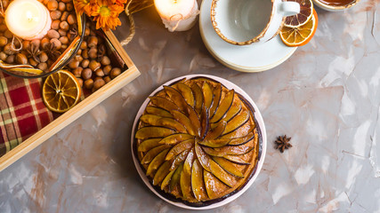 Plum cake decorated with sliced plum among the autumn decor - pumpkin, candle, oranges and yellow chrysanthemum. Rustic style. Homely cozy flat lay. Top view