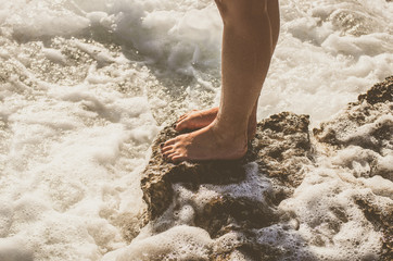 Naked female legs on a rocky cliff washed by sea foam
