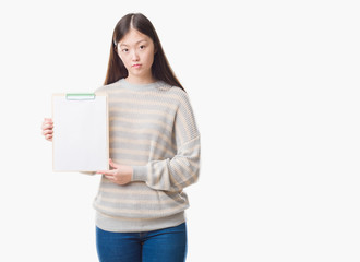 Young Chinese woman over isolated background holding clipboard with a confident expression on smart face thinking serious