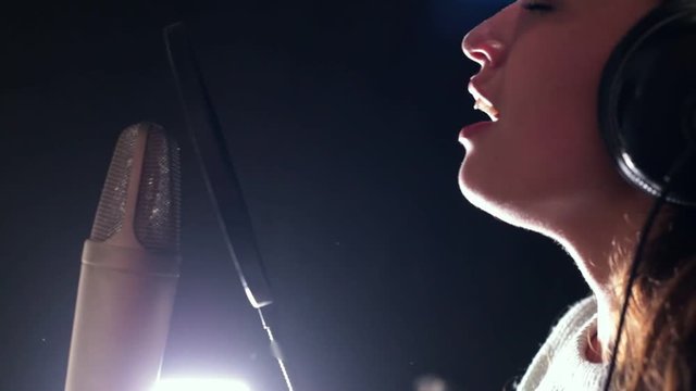 A young attractive woman singing in recording studio, standind near by mic