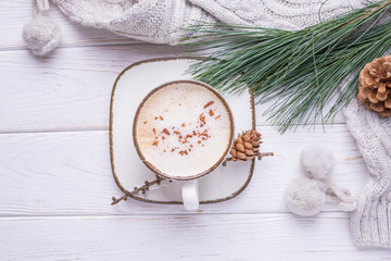 Coffee cappuccino with cinnamon, a branch of a pine tree and knitted accessories on a wooden background. Free space