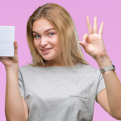 Obraz premium Young caucasian woman holding blank notebook over isolated background doing ok sign with fingers, excellent symbol