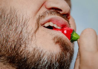 Close-up shows the mouth and teeth of a man biting red hot chili pepper.