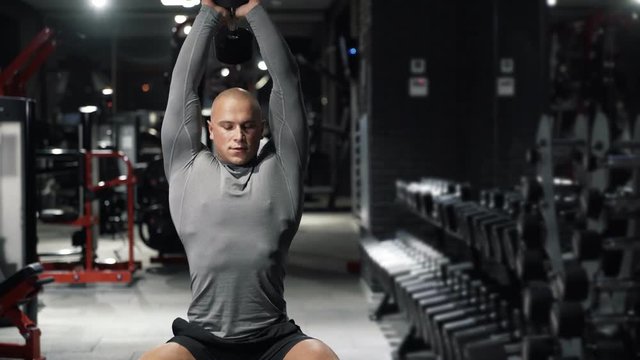 Strong muscular man doing sport exercises with dumbbells, trains the triceps in the dark gym. A sporty guy is engaged in fitness. Concept sport, health.