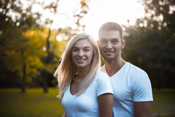 Obraz premium Cute loving couple standing on grass in nature green park with beautiful sundown light. Looking camera.