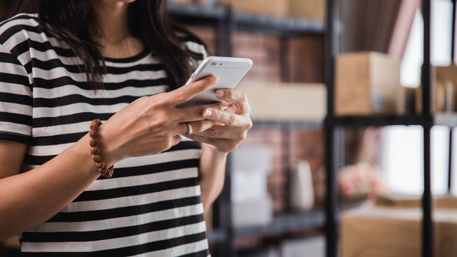 hand using smart phone and packages shelf in background