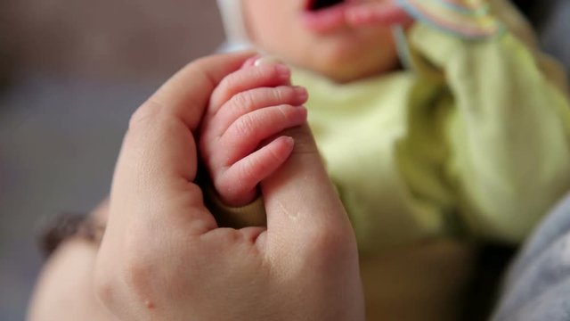 Close-up of mother holding newborn hands. Love and care concept. Baby grasping mom's finger. Hand the sleeping baby in the hand of mother close-up. Close-up of baby's hand holding mother's finger.