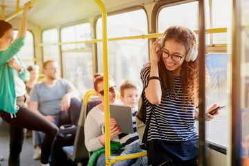 Picture of cute curly girl standing in a public transport and listening to the music.
