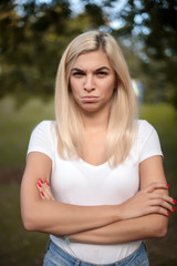 Obraz premium Displeased sad offended beautiful young woman standing on grass in nature green park with beautiful sundown light looking camera.