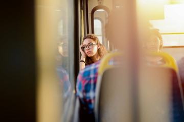 Cute young girl sitting in a bus with her head leaned on window. Looking away.