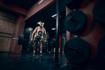 Obraz na płótnie Canvas Muscular caucasian bearded man lifting weights in crossfit gym. Weight plates in front.