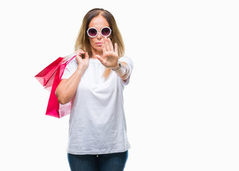 Middle age hispanic woman holding shopping bags on sales over isolated background with open hand doing stop sign with serious and confident expression, defense gesture