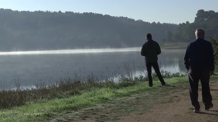 OLD MAN WALKING WHILE ANOTHER MAN WATCHES THE FOG OVER THE LAKE