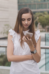 Young european woman holding a mobile phone and looking at its screen. Female entrepreneur checking messages, social feed or browsing