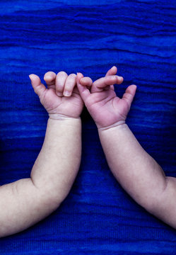 dos manos unidas de dos hermanos gemelos reci&eacute;n nacidos sobre fondo azul