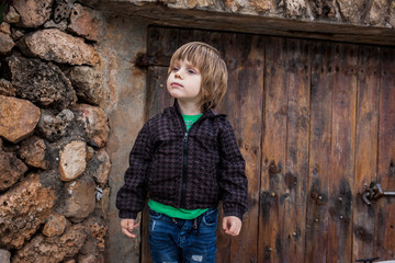 niño rubio con pelo largo sobre fondo de piedra y madera rústico