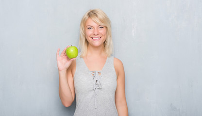 Adult caucasian woman over grunge grey wall eating green apple with a happy face standing and smiling with a confident smile showing teeth