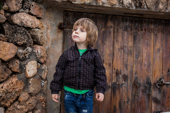 ni&ntilde;o rubio con pelo largo sobre fondo de piedra y madera r&uacute;stico