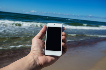 Hand holds smart phone, on beach background