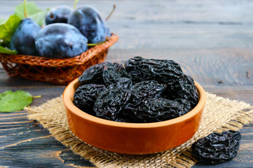 Prunes in a clay bowl and fresh plums, leaves on a wooden table. Fresh prunes for healthy life.