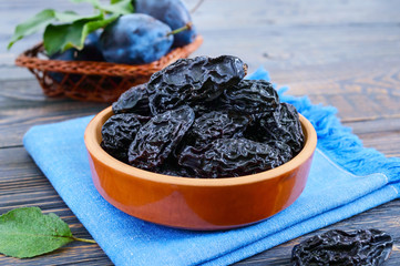 Prunes in a clay bowl and fresh plums, leaves on a wooden table. Fresh prunes for healthy life.