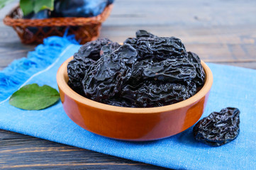 Prunes in a clay bowl and fresh plums, leaves on a wooden table. Fresh prunes for healthy life.