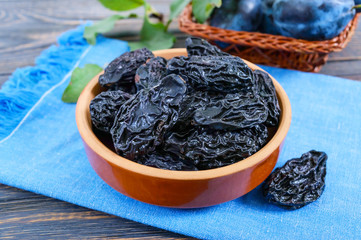 Prunes in a clay bowl and fresh plums, leaves on a wooden table. Fresh prunes for healthy life.