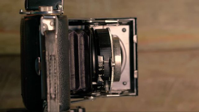eine alte Kamera mit Klappbalgen wird ge&ouml;ffnet, das Objektiv f&auml;hrt aus und der Ausl&ouml;ser wird gedr&uuml;ckt